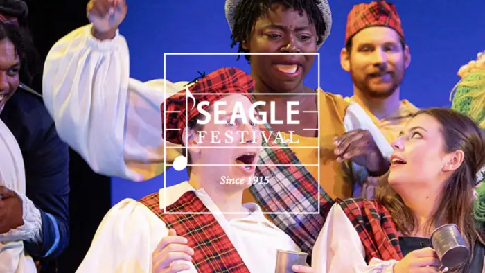 People on stage wearing plaid sashes over white shirts project their voices into the crowd.